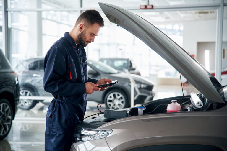 Angestellter überprüft die technischen Daten eines Autos mit einem Tablet und einem Auslesegerät – präzise Diagnose und Wartung im Automobilbereich.