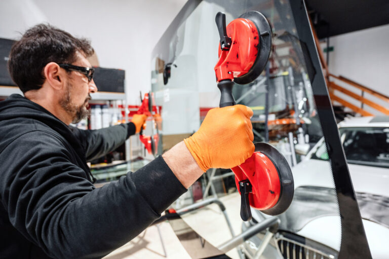 Ein Kursteilnehmer setzt eine neue Glasscheibe ein in einem silbernen Auto.